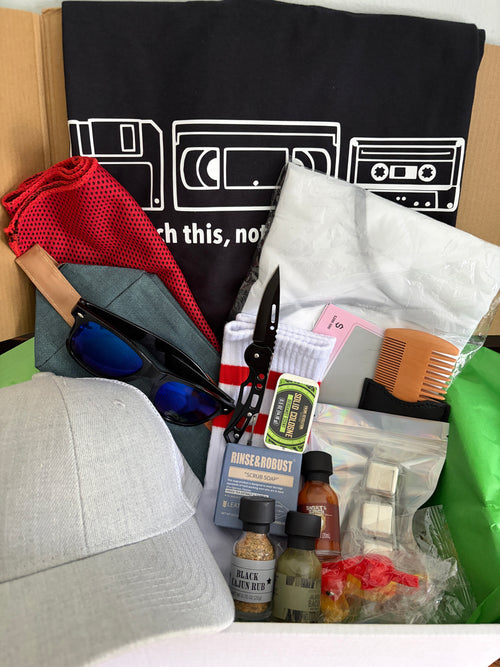 Collection of items including a black t-shirt with white graphics, sunglasses, a red towel, and small bottles on a white surface.